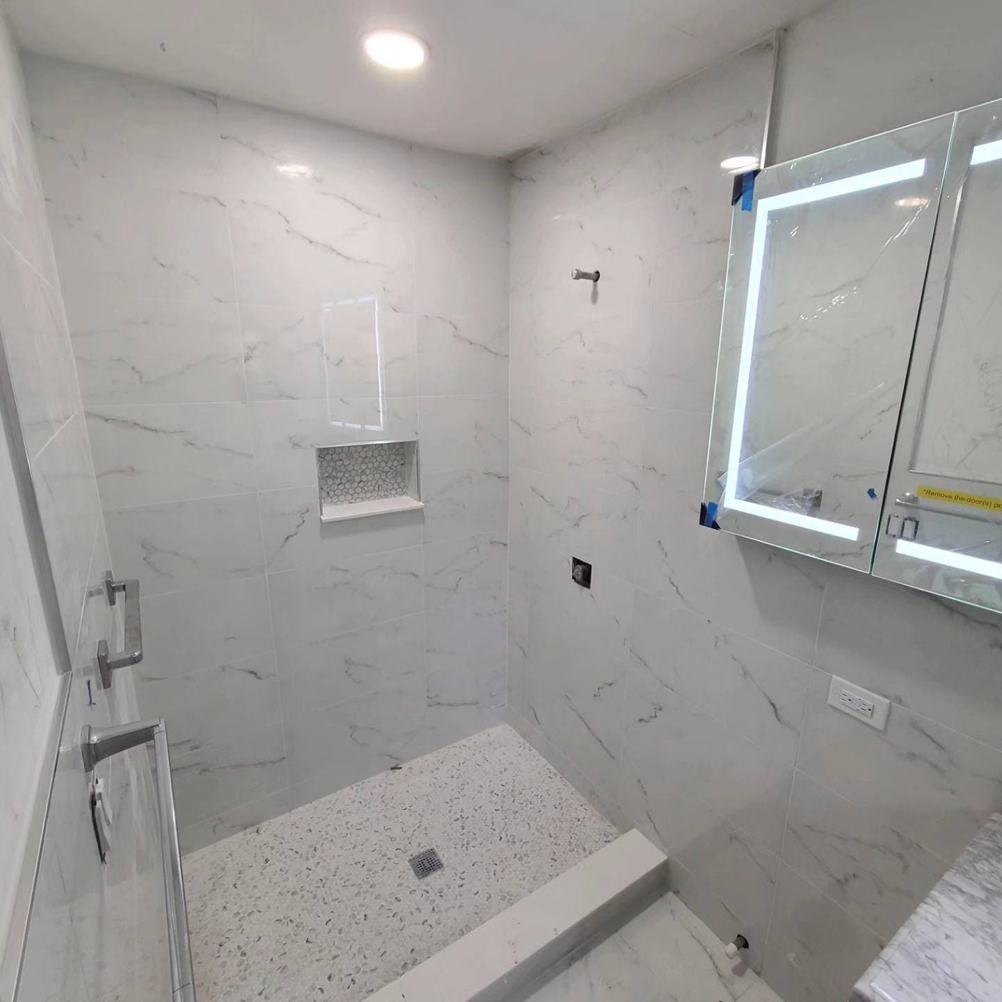 KJB Construction walk-in shower with marble tile, glass door, and LED mirror