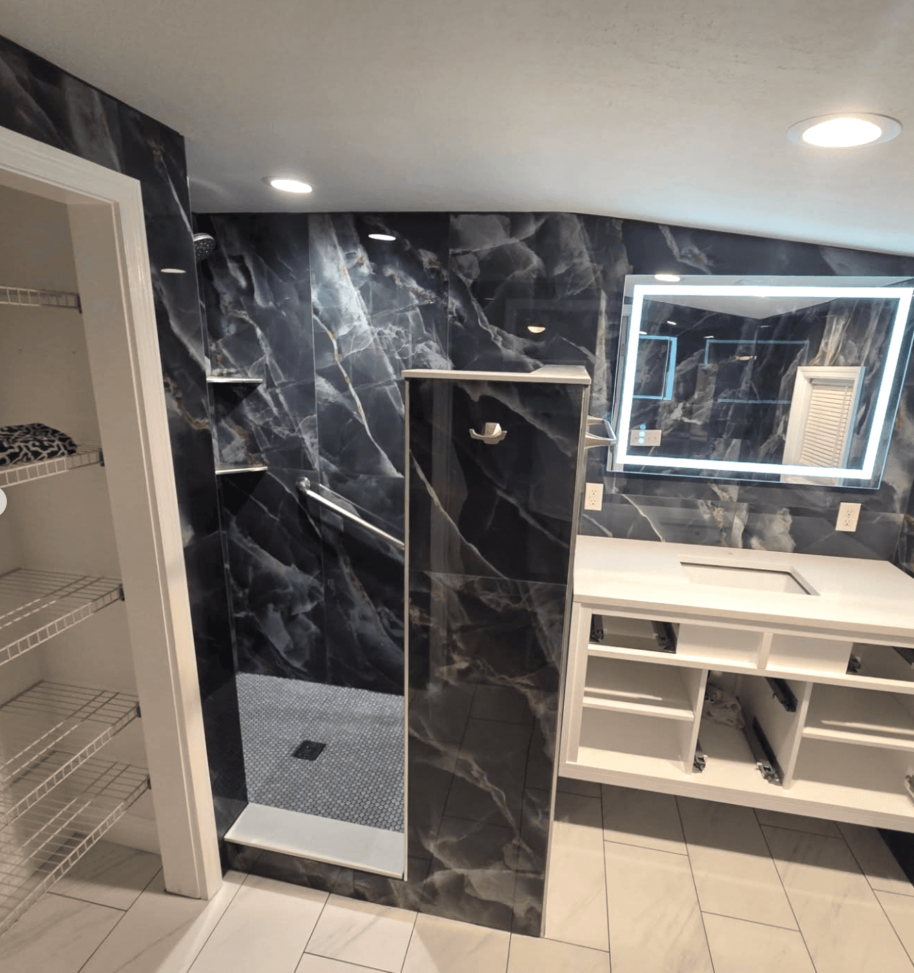 KJB Construction full black marble bathroom with glass walk-in shower, white vanity, and closet