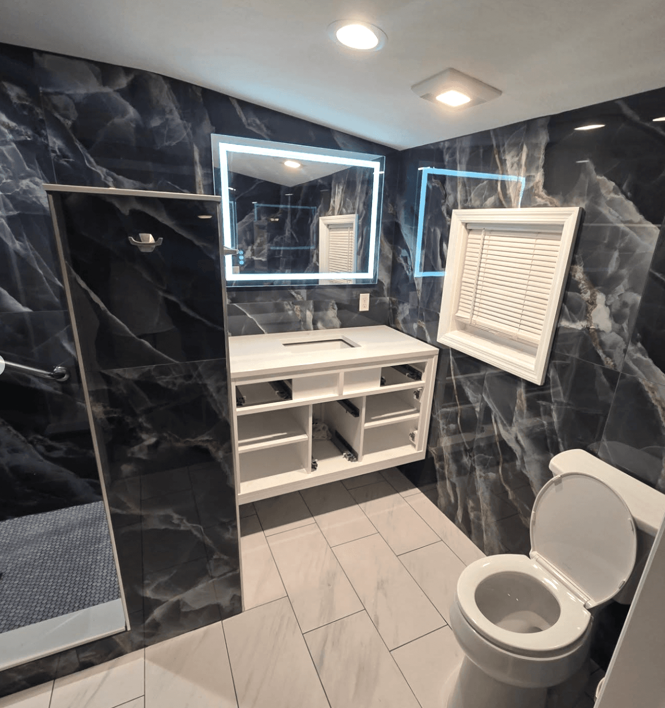 KJB Construction bathroom with dramatic black marble walls, white floating vanity, and LED mirror