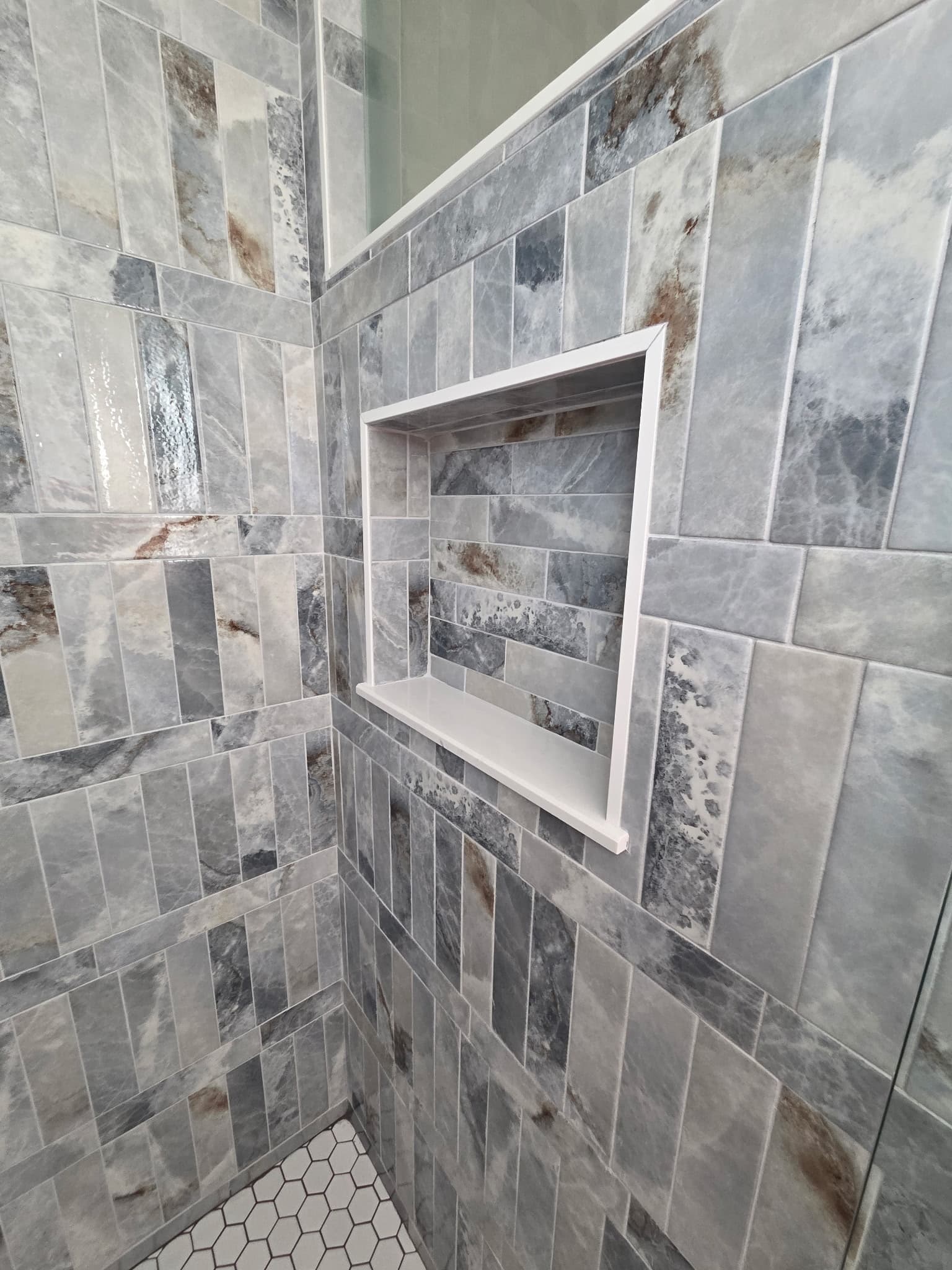 KJB Construction shower niche detail with blue-grey natural stone subway tile in stacked pattern and white hexagonal floor tile