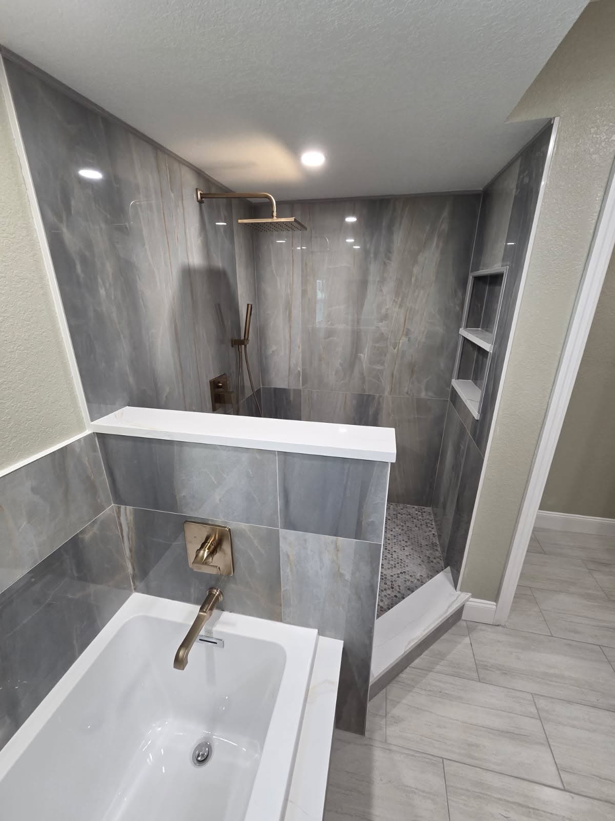 KJB Construction full master bath view with soaking tub, brass rain shower, and built-in niches