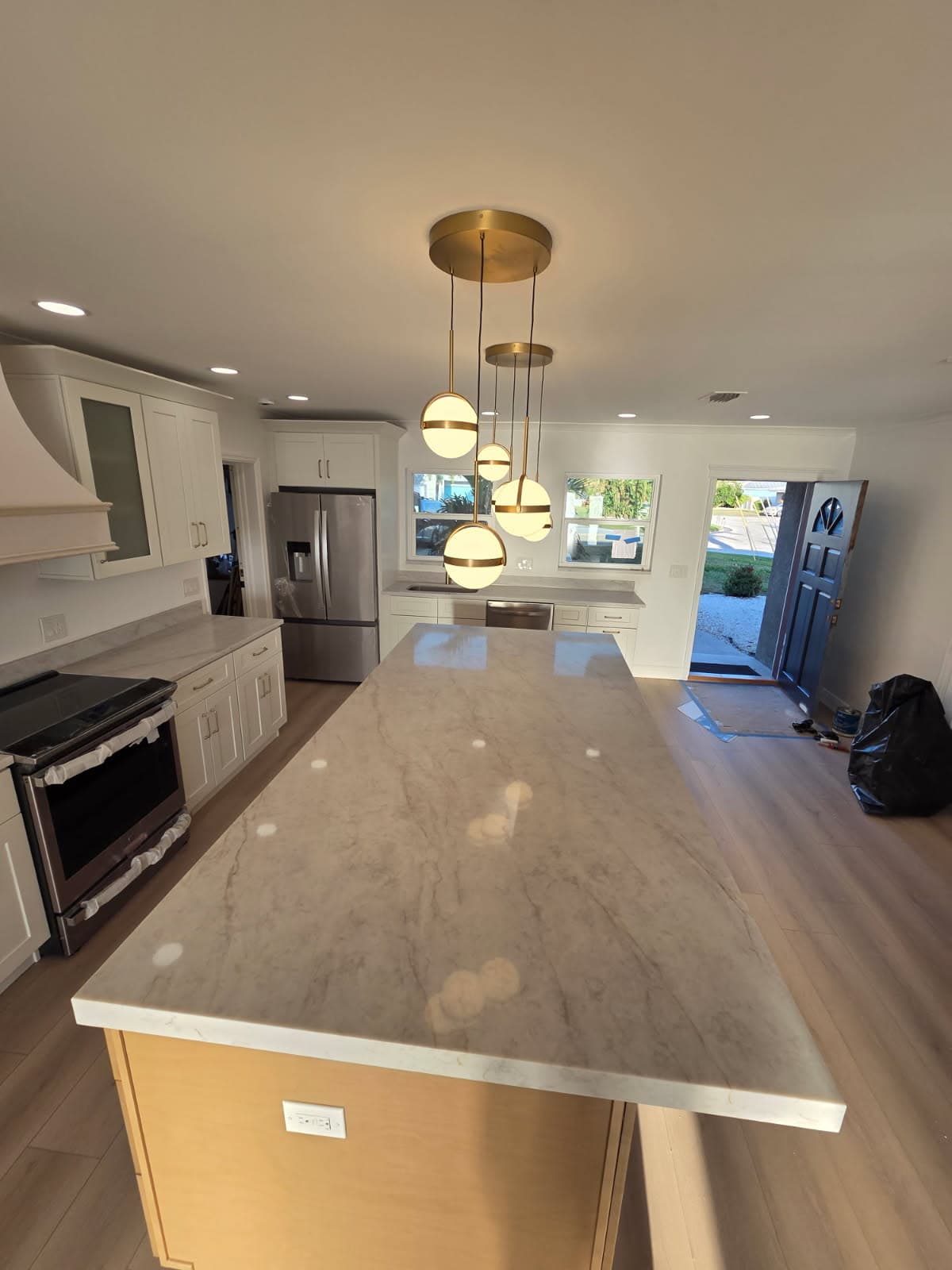 KJB Construction kitchen island with marble countertop, brass globe pendants, white cabinets with range hood, and front door entry view