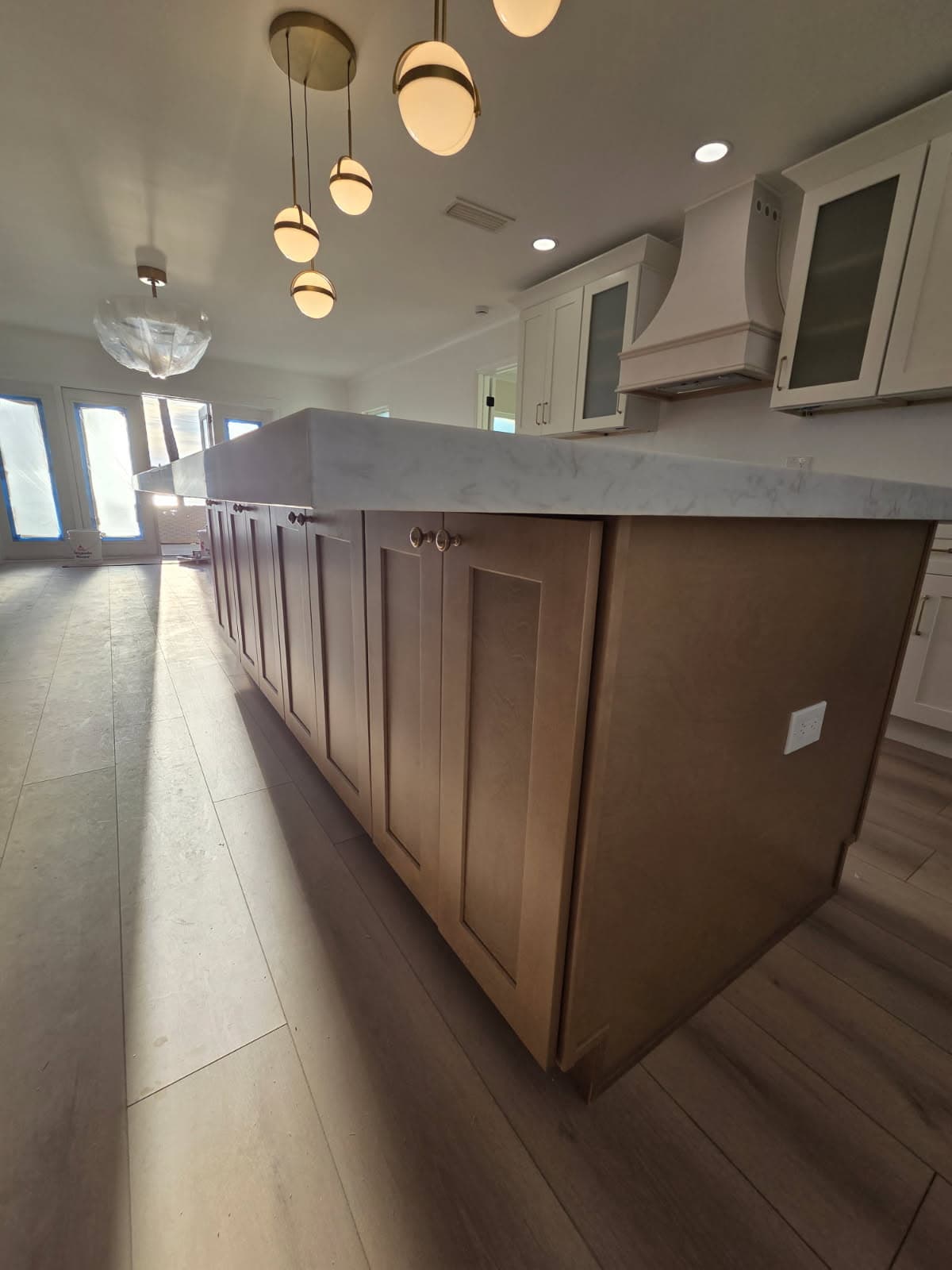 KJB Construction kitchen island low angle showing birch shaker cabinets, marble countertop, brass globe pendants, and white perimeter cabinetry