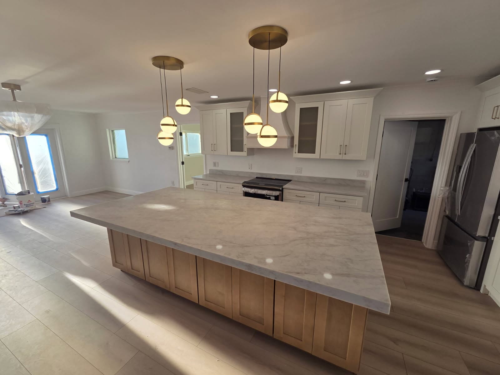 KJB Construction open kitchen with large birch island, marble countertop, brass globe pendant lights, and white shaker perimeter cabinets