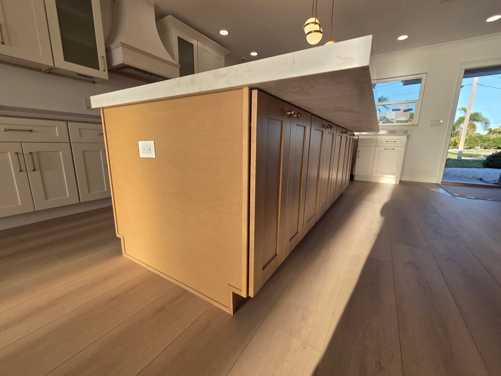 KJB Construction waterfront kitchen birch island side view with marble countertop overhang, white perimeter cabinets, and brass pendants