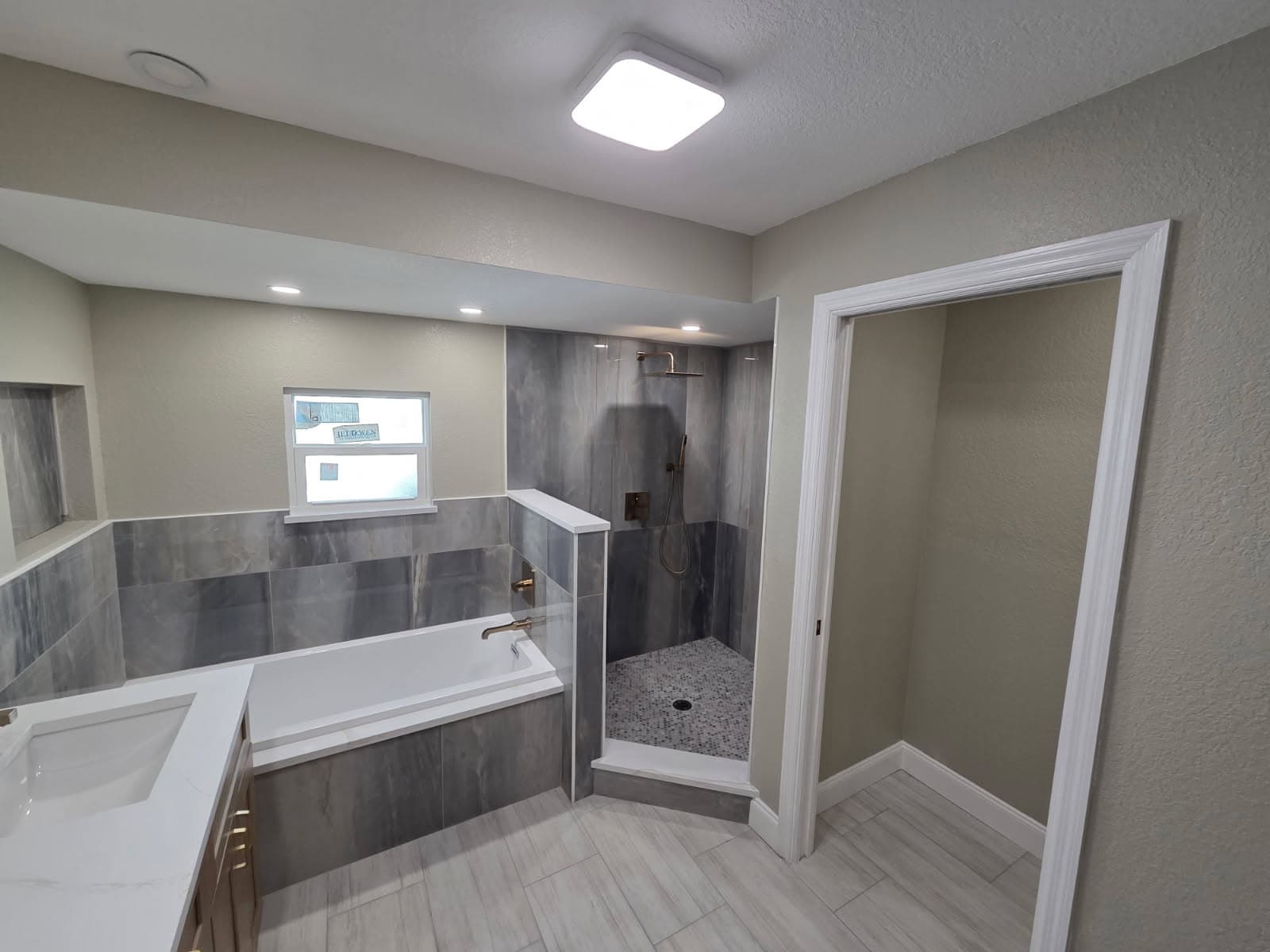KJB Construction complete master bathroom with grey marble, soaking tub, walk-in shower, and closet entry