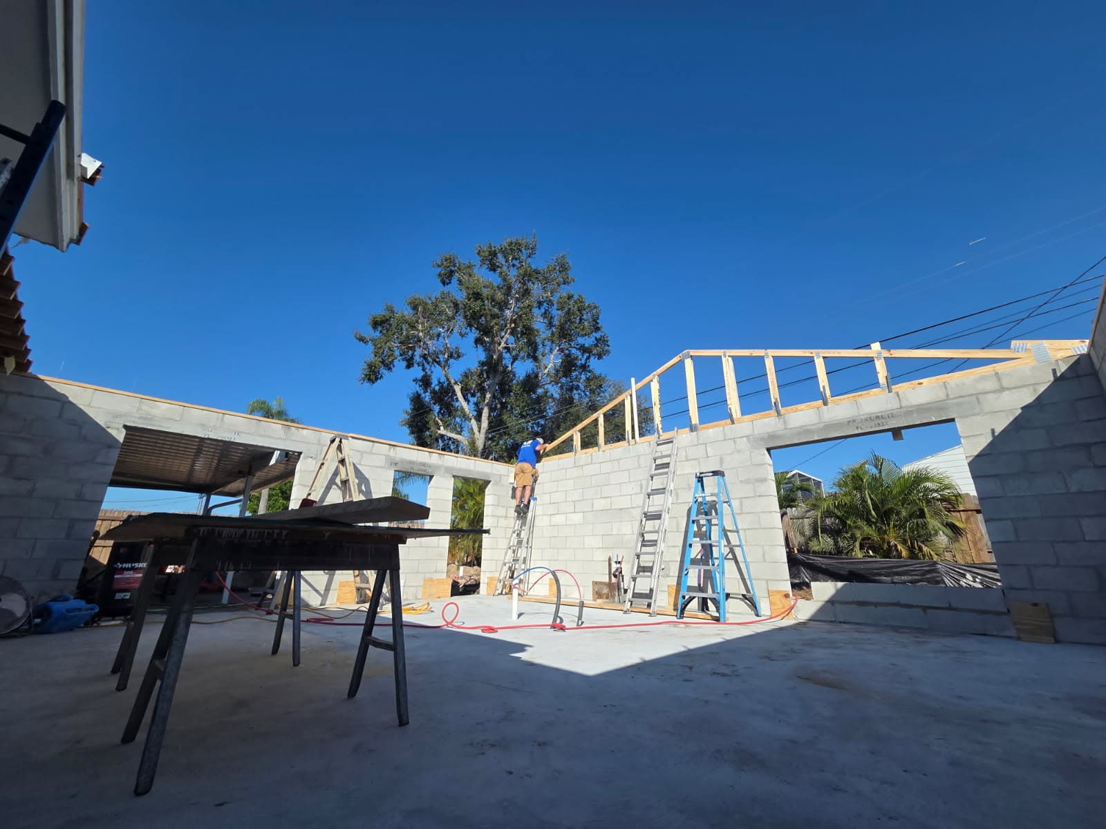 KJB Construction new build with concrete block walls, wood roof trusses, and crew on ladders under clear blue sky