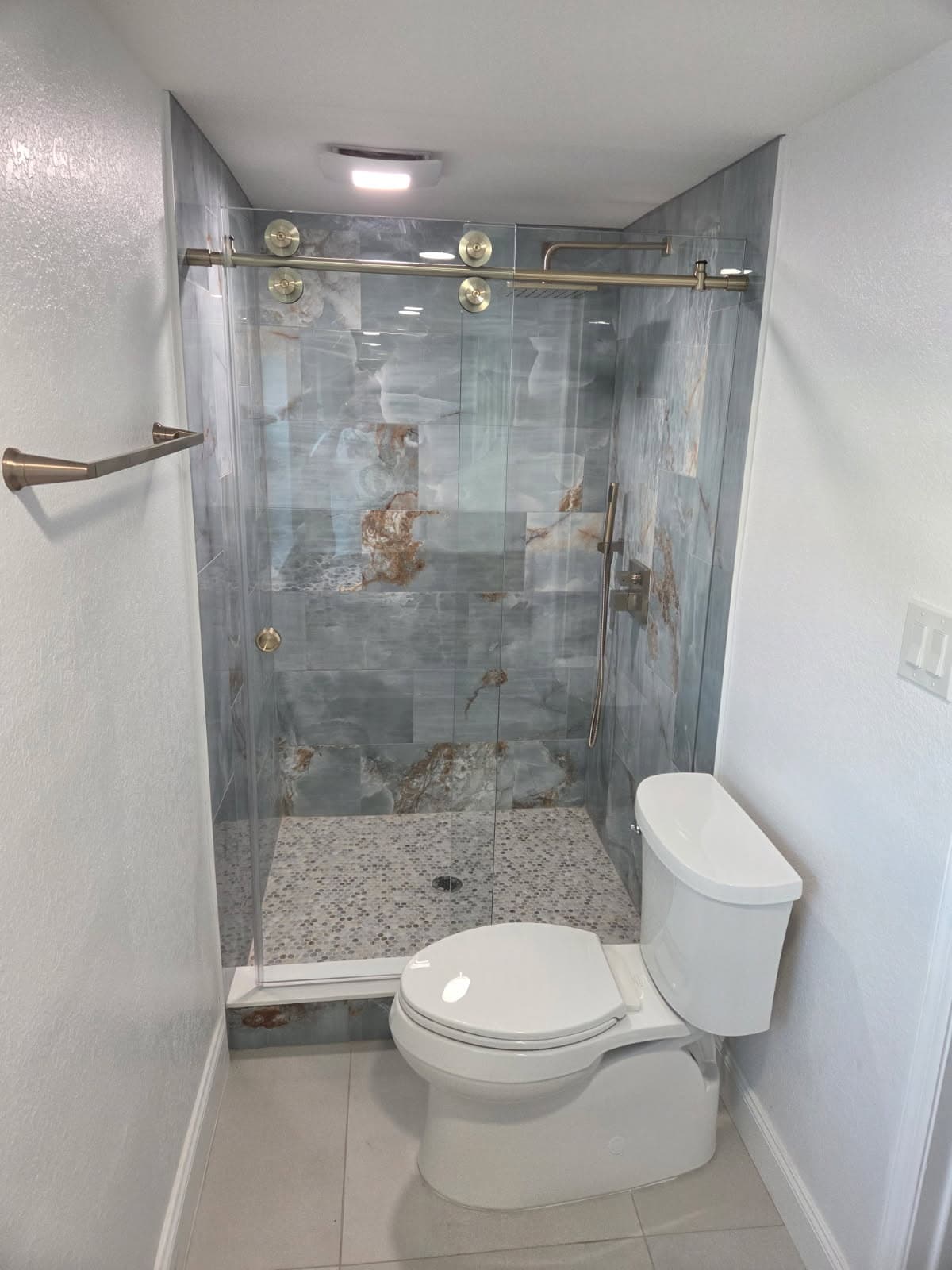 KJB Construction walk-in shower with blue-grey onyx porcelain tile, brass sliding glass door, and pebble mosaic floor