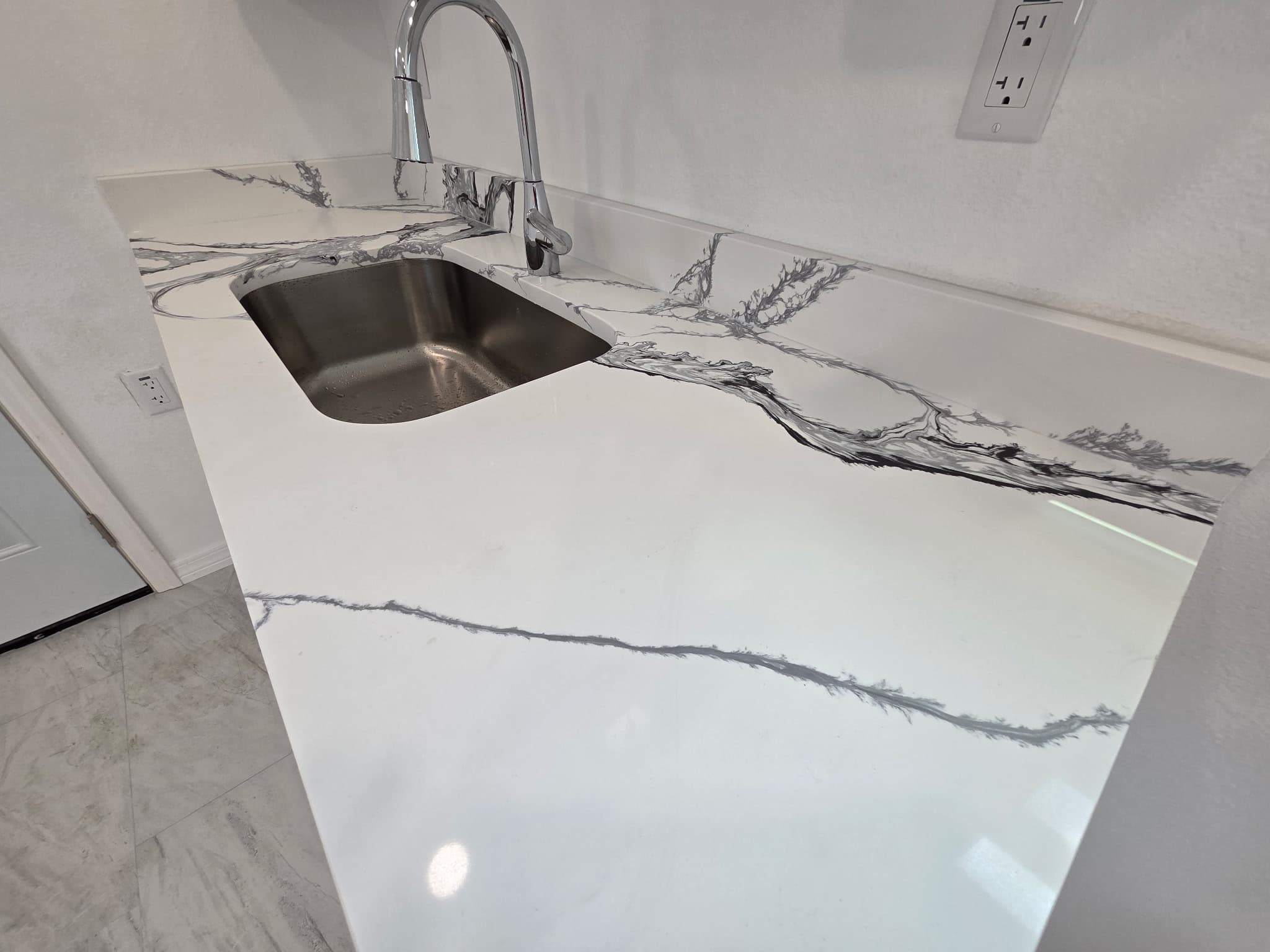 KJB Construction white quartz countertop closeup with dramatic grey veining, undermount stainless sink, and chrome gooseneck faucet