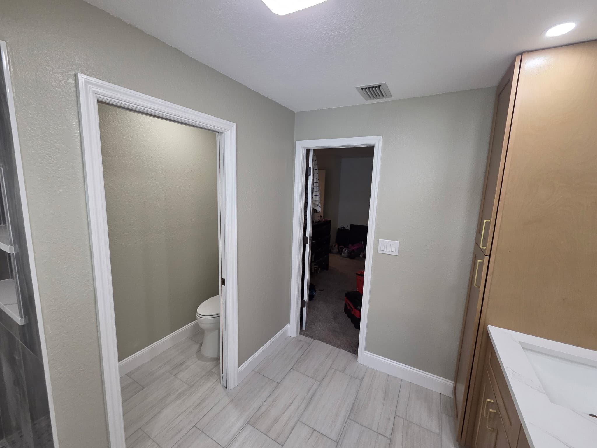 KJB Construction sage green bathroom with wood-look tile floor, enclosed toilet room, wood linen tower, and white trim