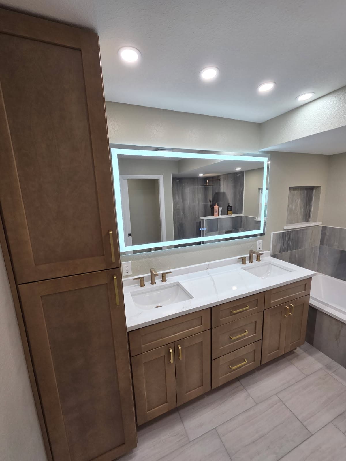 KJB Construction double vanity with tall linen tower, LED backlit mirror, and brass fixtures