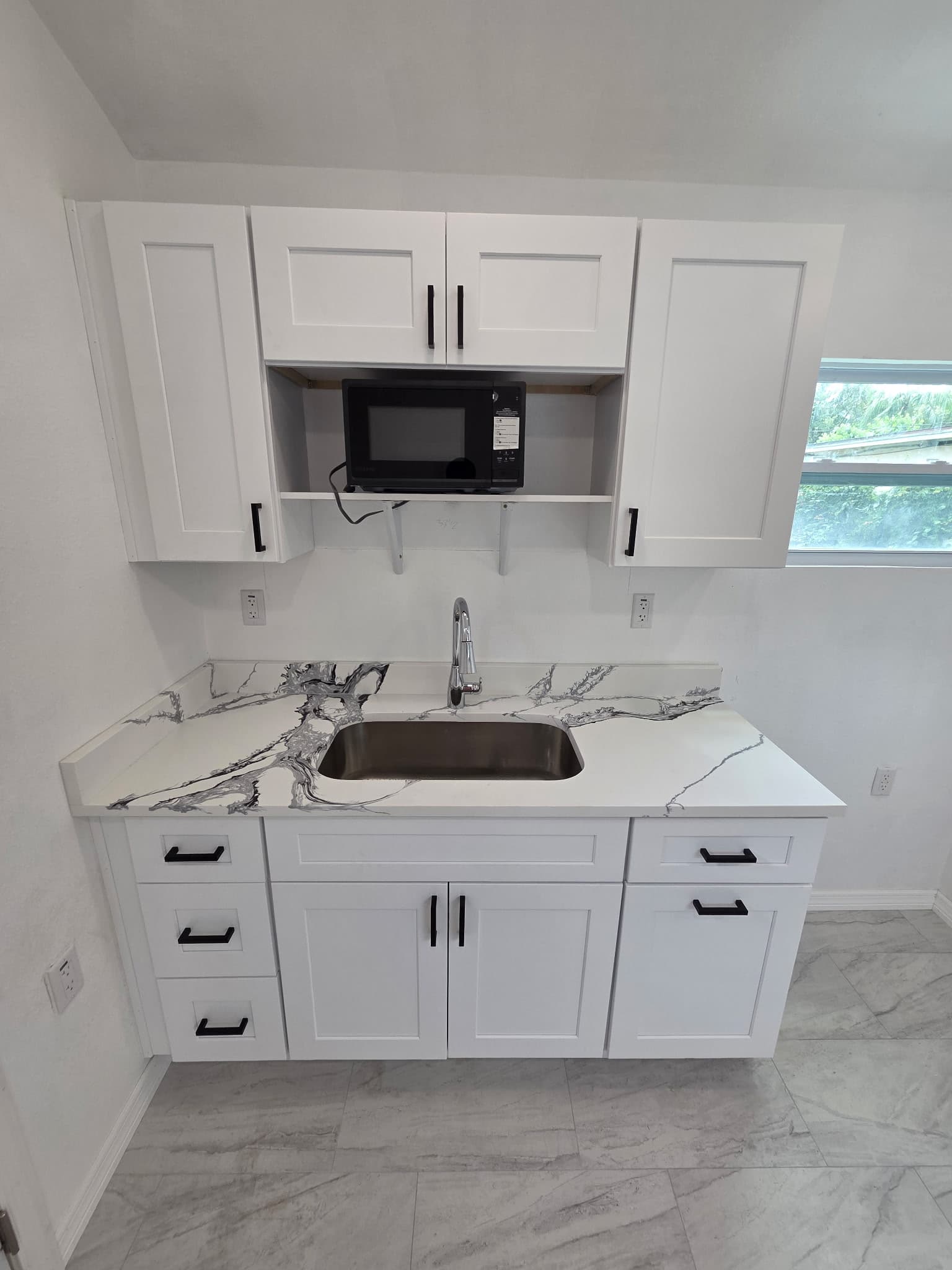 KJB Construction white shaker kitchenette with marble-veined quartz countertop, undermount sink, black hardware, and built-in microwave