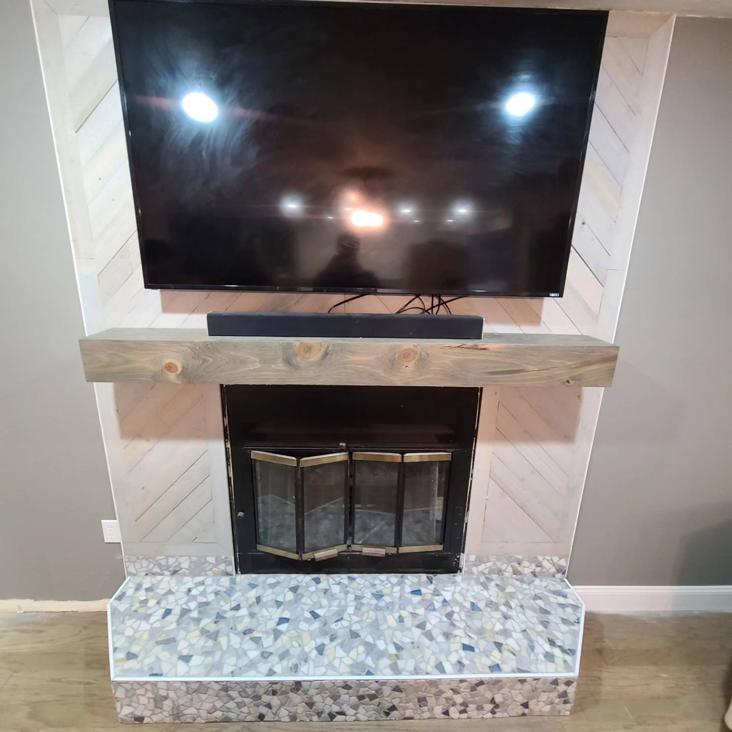 Living room fireplace with white shiplap, wood mantel, and decorative tile hearth